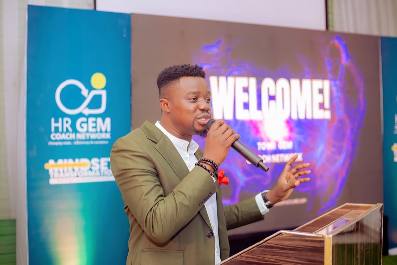 The host welcoming guests at the podium in front of a "Welcome!" screen