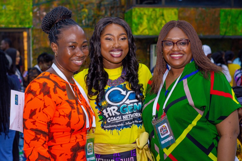 Three women smiling together, one in a yellow HR GEMs T-shirt
