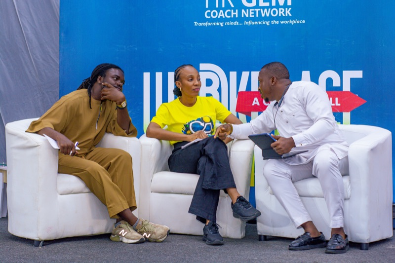 Three speakers in conversation on white sofas on stage