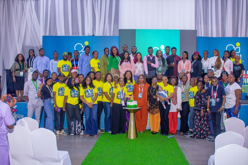 A large group of attendees, many in yellow HR GEMs T-shirts, posing together in front of the stage